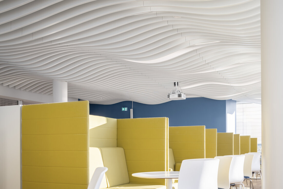 img-de-boehringer-biberach-14 Moderne Kantine im Bürogebäude mit markanter Lamellendecke von Lindner und gelben Sitznischen für eine inspirierende Pausenatmosphäre.