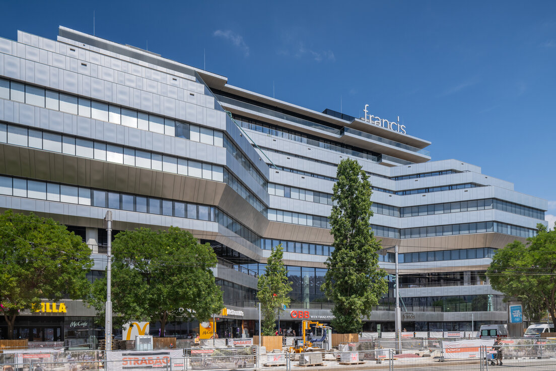 © © Walter Luttenberger Außenansicht des Bürogebäudes Francis im Althan Quartier Wien mit moderner silberner Glasfassade, großen Fensterflächen und Bäumen im Vordergrund | © © Walter Luttenberger