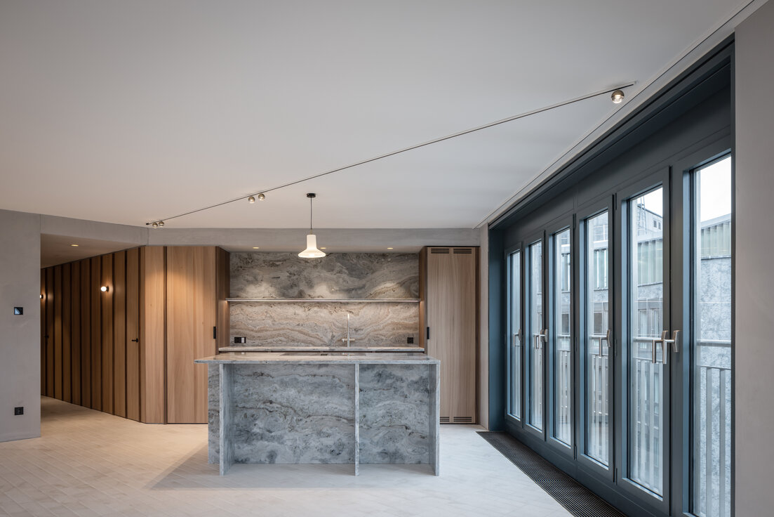 © © www.Lindner-Group.com Moderner Küchenbereich mit heller Marmor-Kücheninsel, Fensterfront und hochwertiger Holzvertäfelung in stilvollem Innenraum | © © www.Lindner-Group.com