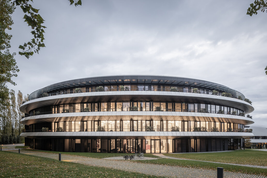 © © www.Lindner-Group.com Außenansicht des ringförmigen Gebäudes „The Doughnut“ am Institut Le Rosey in der Schweiz mit Grünflächen und Gehwegen. | © © www.Lindner-Group.com