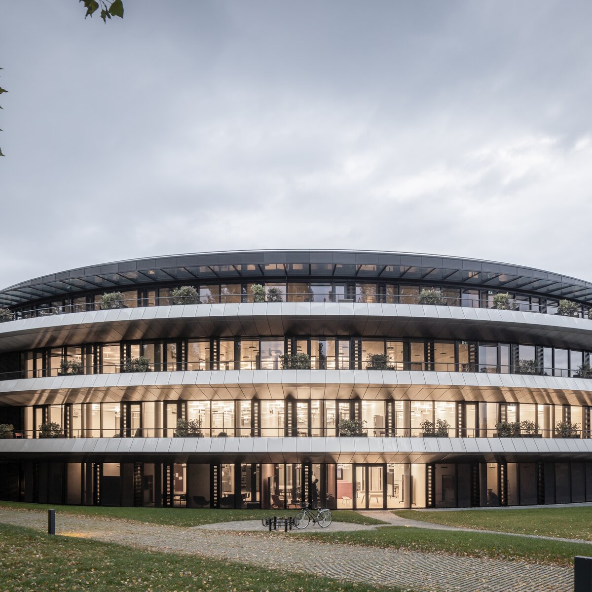 © © www.Lindner-Group.com Außenansicht des ringförmigen Gebäudes „The Doughnut“ am Institut Le Rosey in der Schweiz mit Grünflächen und Gehwegen. | © © www.Lindner-Group.com