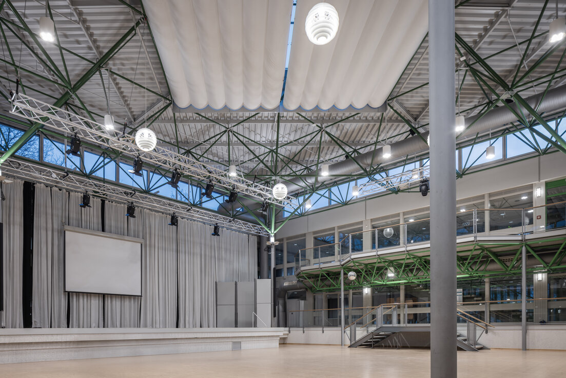 © © www.Lindner-Group.com Atrium des Gymnasiums Vilshofen mit hängenden Leuchten, Bühne und Leinwand im multifunktionalen Veranstaltungsraum. | © © www.Lindner-Group.com