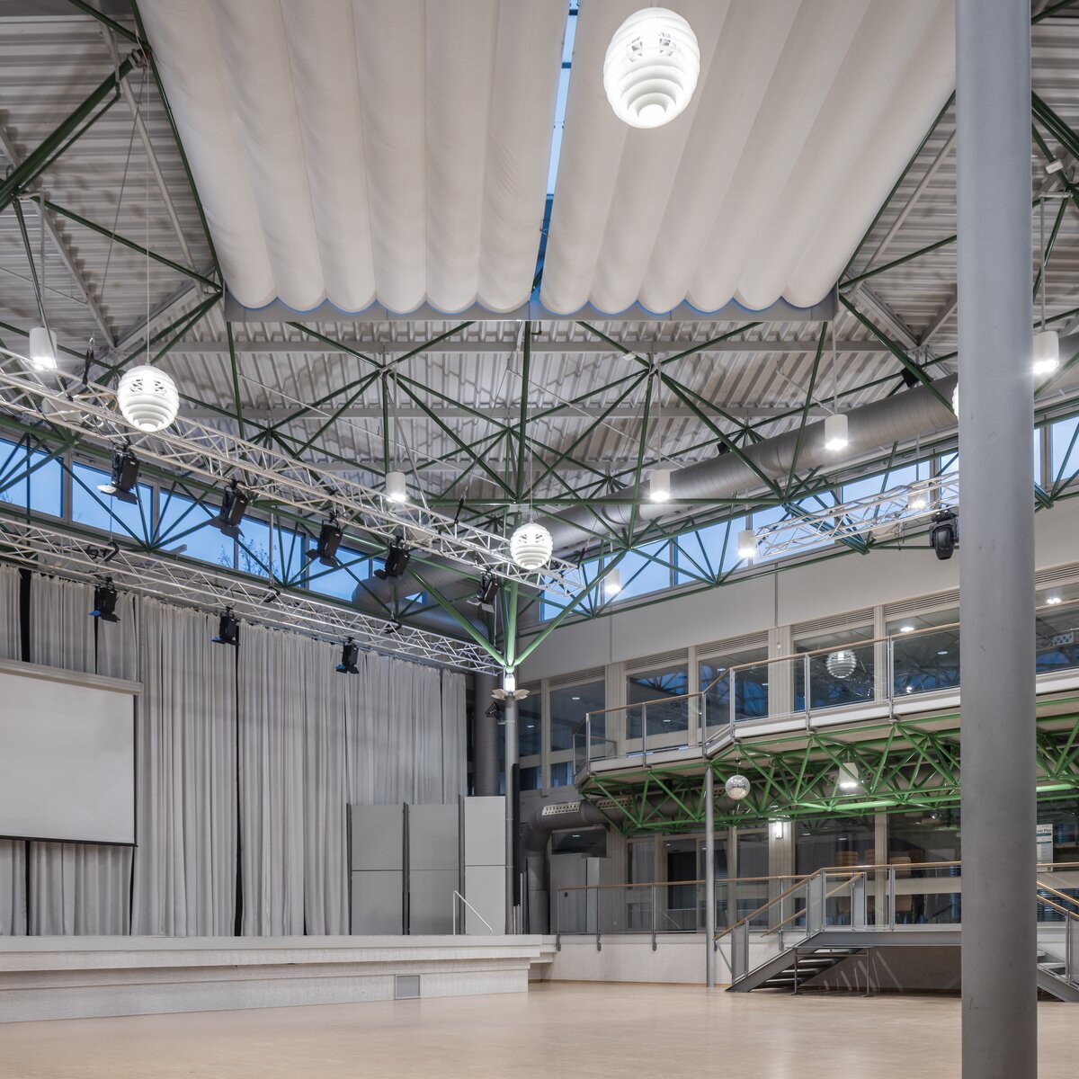 © © www.Lindner-Group.com Atrium des Gymnasiums Vilshofen mit hängenden Leuchten, Bühne und Leinwand im multifunktionalen Veranstaltungsraum. | © © www.Lindner-Group.com